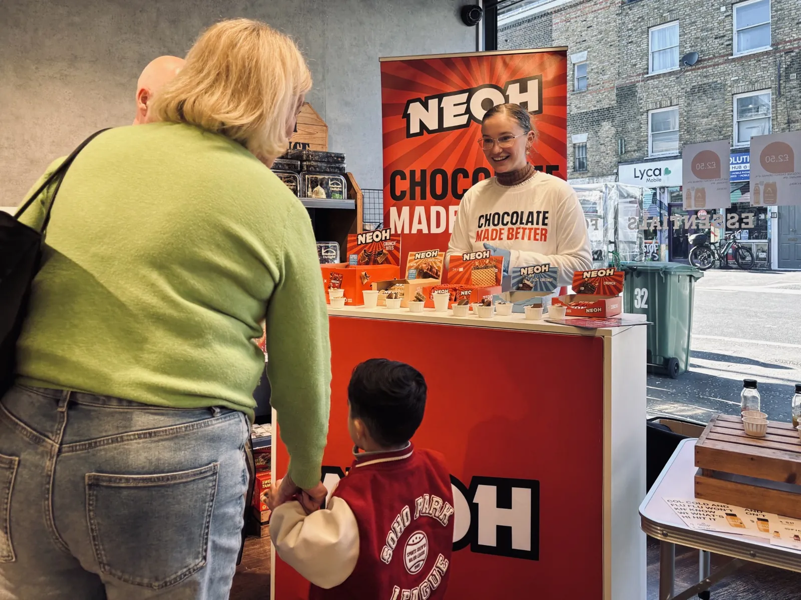 FOTS brand ambassador offering NEOH chocolate samples to shoppers at an in-store tasting counter in a London convenience store